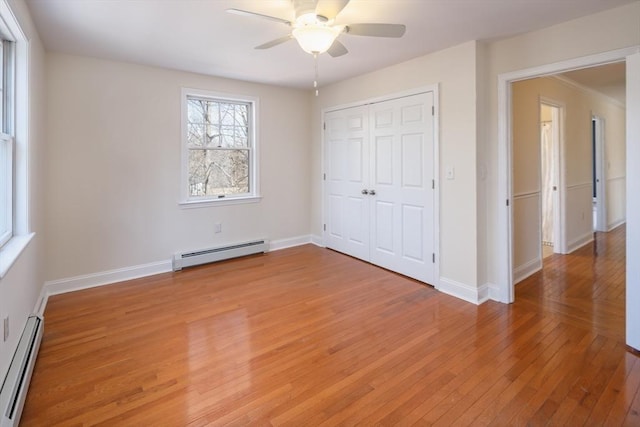 unfurnished bedroom featuring light wood finished floors, baseboard heating, a closet, and baseboards