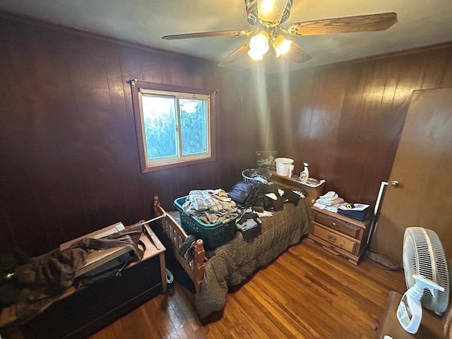 bedroom with wooden walls, ceiling fan, and wood-type flooring