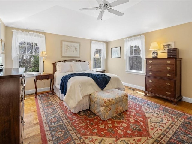 bedroom featuring light wood finished floors, multiple windows, baseboards, and vaulted ceiling