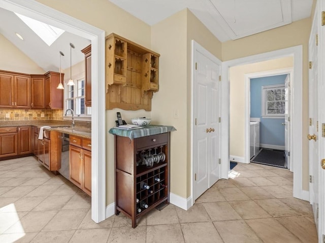 bar area featuring a skylight, backsplash, washer / clothes dryer, vaulted ceiling, and pendant lighting