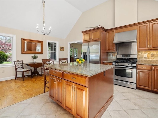 kitchen featuring stainless steel appliances, wall chimney range hood, a kitchen island, brown cabinetry, and tasteful backsplash