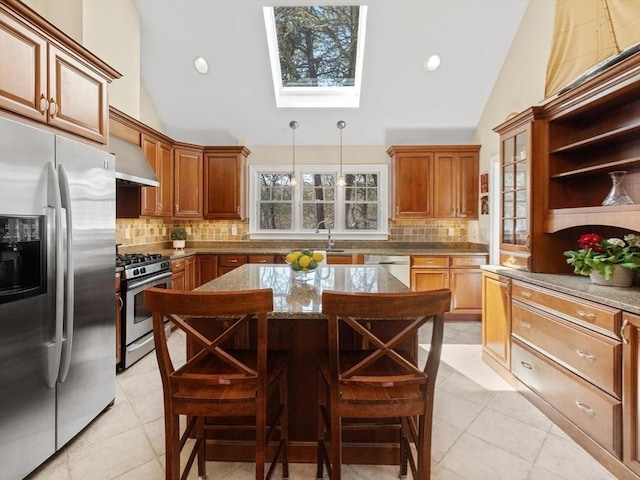kitchen with stainless steel appliances, a skylight, wall chimney range hood, a center island, and tasteful backsplash