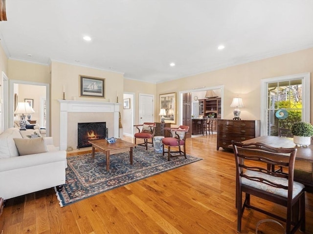 living area featuring crown molding, a fireplace with flush hearth, wood finished floors, and recessed lighting