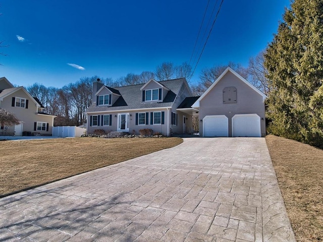 cape cod home with an attached garage, fence, decorative driveway, a chimney, and a front yard