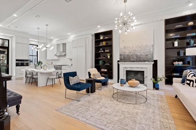 living room with built in features, a fireplace, a chandelier, crown molding, and light hardwood / wood-style flooring