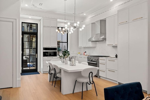 kitchen with wall chimney range hood, a center island, light hardwood / wood-style floors, white cabinets, and oven