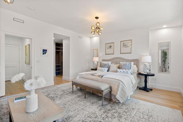 bedroom with an inviting chandelier, a walk in closet, a closet, and light wood-type flooring