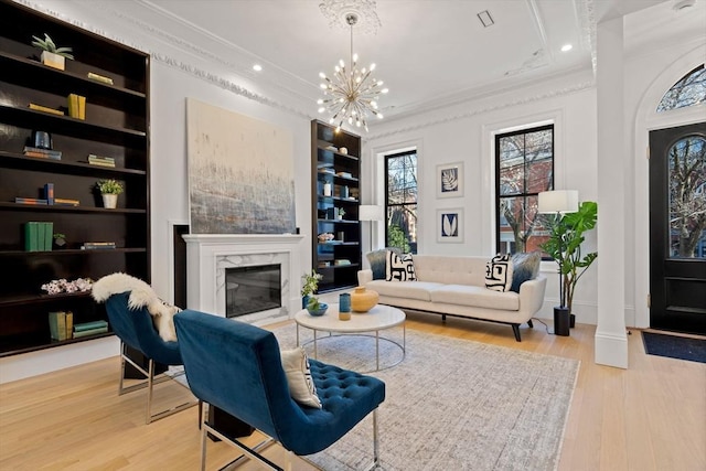 sitting room with a chandelier, light wood-type flooring, ornamental molding, built in features, and a premium fireplace