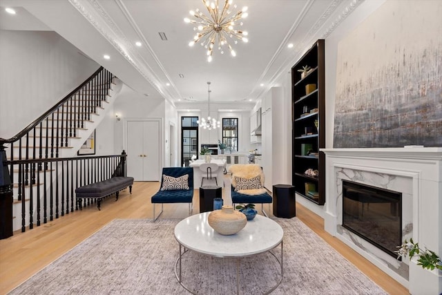 living room featuring a premium fireplace, light wood-type flooring, an inviting chandelier, and built in shelves