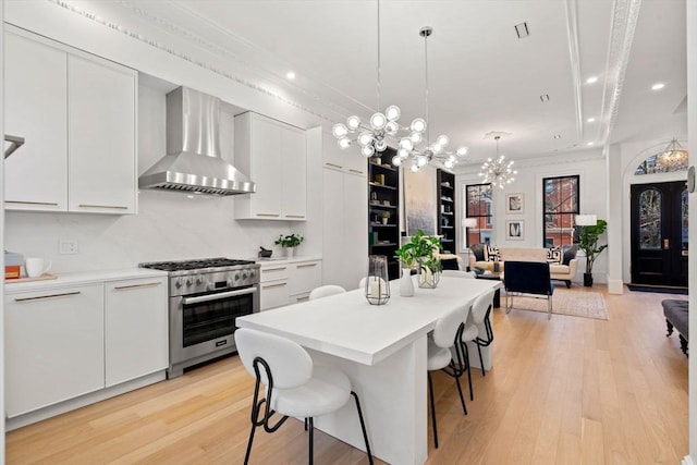 kitchen with white cabinetry, wall chimney exhaust hood, high end stainless steel range, and a chandelier