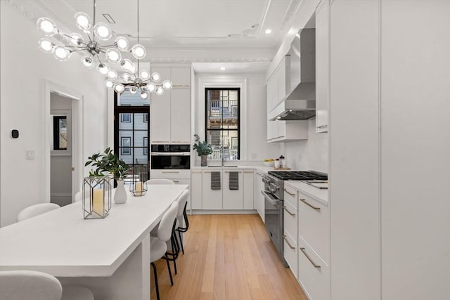 kitchen with wall chimney exhaust hood, a breakfast bar, stainless steel range, light hardwood / wood-style floors, and white cabinets