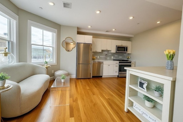 89 Prescott St Unit C, Boston, MA 02128 - kitchen featuring stainless steel appliances, white cabinets, backsplash, light countertops, and light wood-style flooring