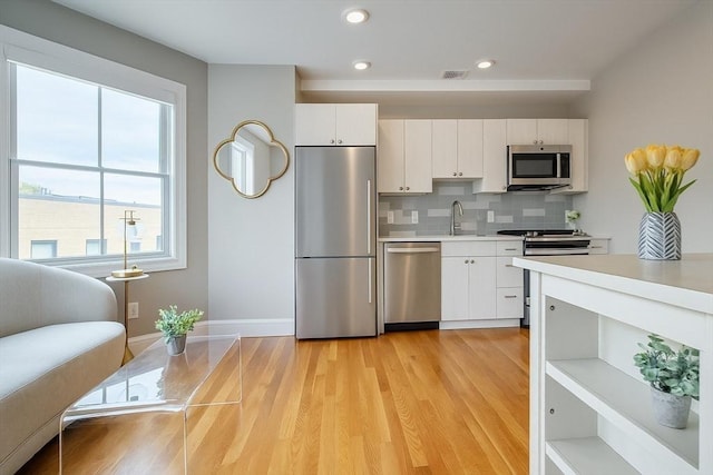 89 Prescott St Unit C, Boston, MA 02128 - kitchen with appliances with stainless steel finishes, light countertops, decorative backsplash, white cabinetry, and light wood finished floors