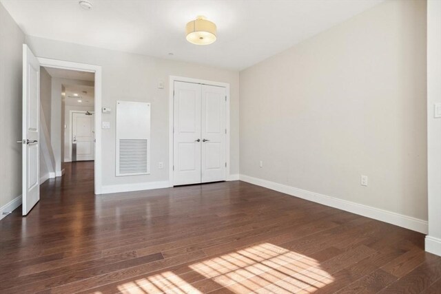 unfurnished bedroom with dark wood-style floors, a closet, and baseboards