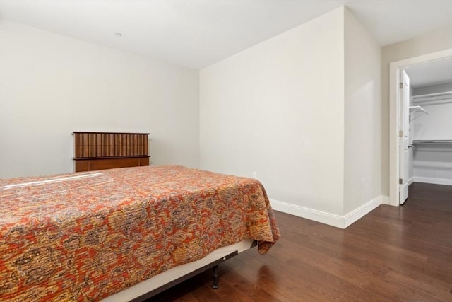 bedroom featuring a spacious closet, wood finished floors, and baseboards