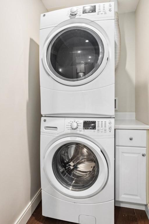 laundry room featuring cabinet space, stacked washer / drying machine, baseboards, and dark wood-style flooring