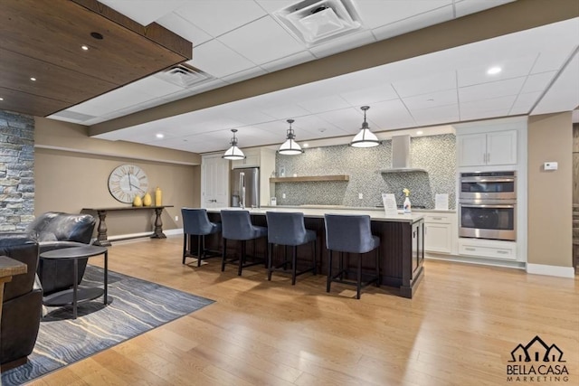 kitchen with visible vents, open floor plan, light wood-type flooring, stainless steel appliances, and wall chimney exhaust hood