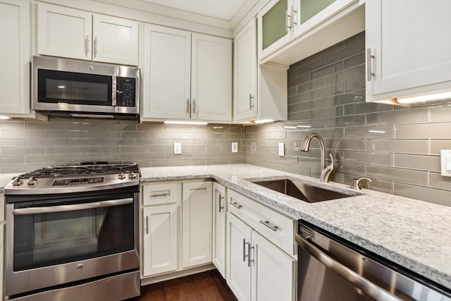 kitchen with a sink, backsplash, white cabinetry, stainless steel appliances, and light stone countertops