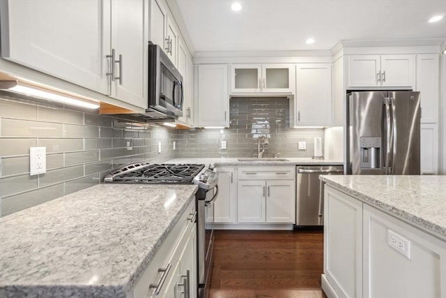 kitchen featuring a sink, light stone counters, appliances with stainless steel finishes, white cabinets, and decorative backsplash