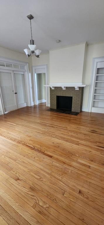 unfurnished living room with an inviting chandelier, a brick fireplace, built in features, and light wood-type flooring