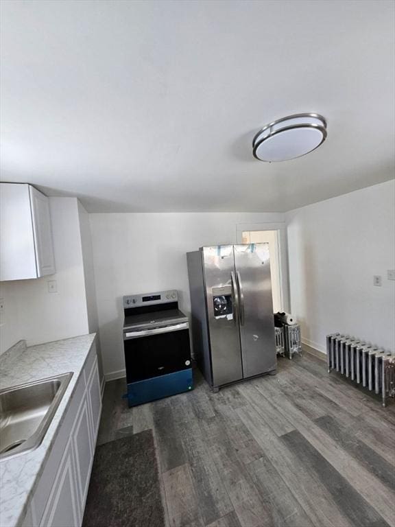 kitchen with sink, radiator, dark wood-type flooring, appliances with stainless steel finishes, and white cabinetry