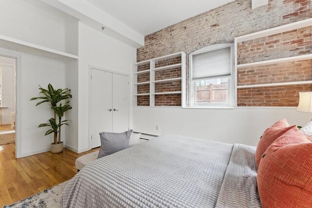 69 Harvey St Unit 1, Cambridge, MA 02140 - bedroom with brick wall, wood finished floors, a closet, baseboard heating, and baseboards