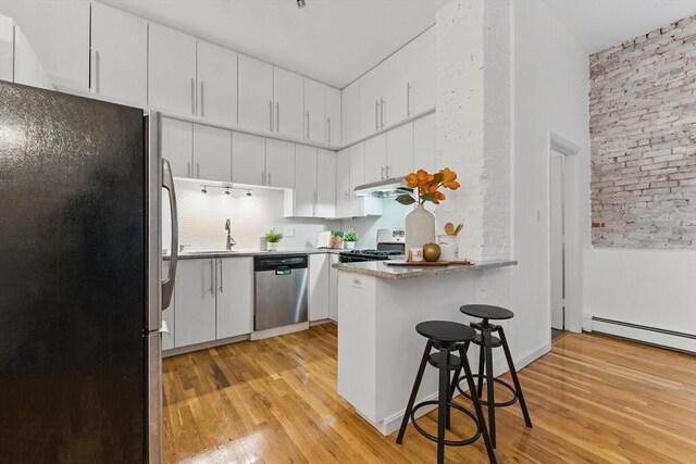 69 Harvey St Unit 1, Cambridge, MA 02140 - kitchen with stainless steel appliances, a peninsula, light wood-style flooring, brick wall, and white cabinetry