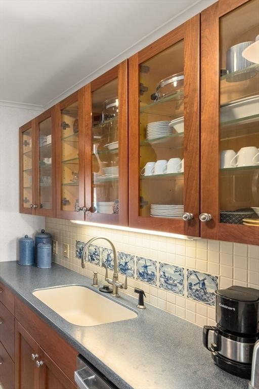 interior space with dark countertops, glass insert cabinets, brown cabinets, a sink, and backsplash