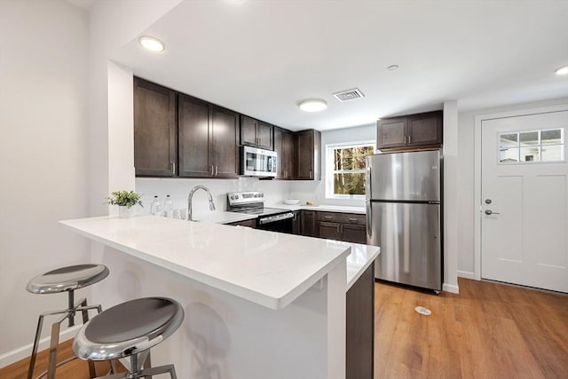 kitchen featuring light wood-type flooring, a kitchen breakfast bar, dark brown cabinetry, and stainless steel appliances