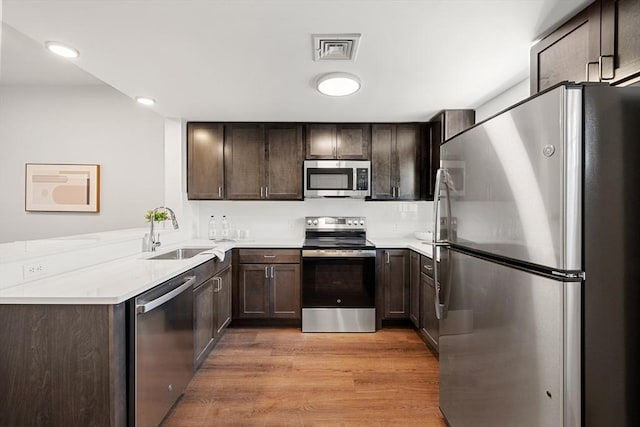 kitchen featuring dark brown cabinetry, sink, stainless steel appliances, light hardwood / wood-style flooring, and kitchen peninsula