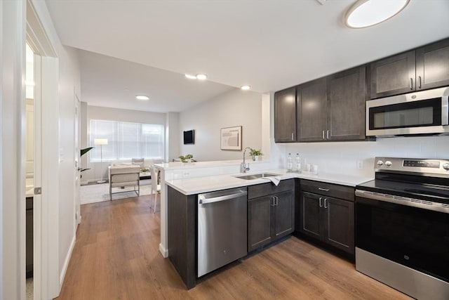 kitchen with sink, kitchen peninsula, dark brown cabinetry, wood-type flooring, and stainless steel appliances