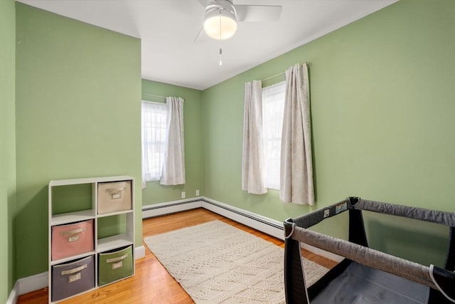 bedroom featuring multiple windows, hardwood / wood-style floors, ceiling fan, and baseboard heating