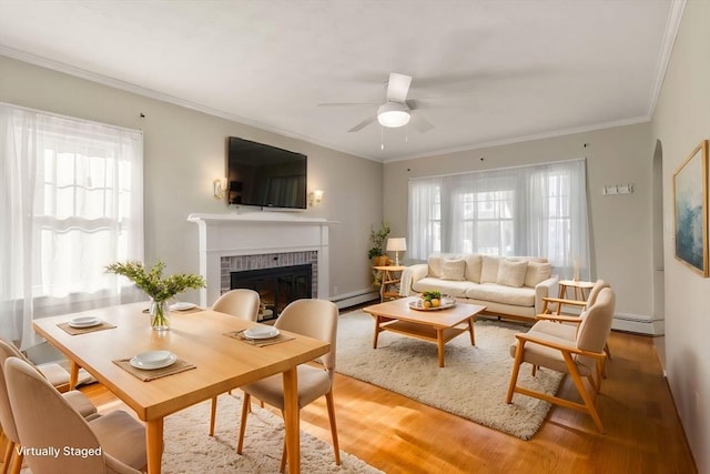 living room with crown molding, ceiling fan, a baseboard heating unit, a brick fireplace, and light wood-type flooring