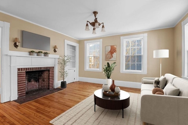 living room featuring built in shelves, a brick fireplace, ornamental molding, a notable chandelier, and hardwood / wood-style flooring