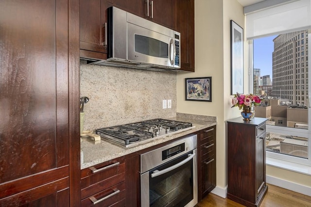 kitchen with a city view, stainless steel appliances, backsplash, dark brown cabinetry, and wood finished floors