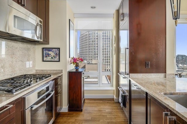 kitchen featuring light stone counters, stainless steel appliances, backsplash, wood finished floors, and baseboards