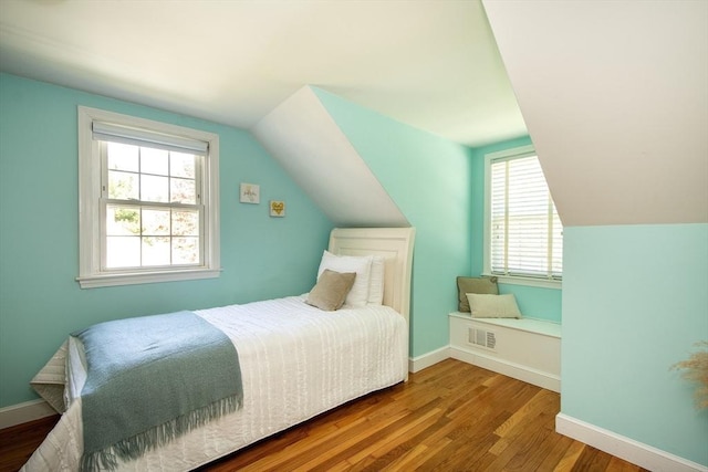 bedroom with baseboards, visible vents, wood finished floors, and lofted ceiling