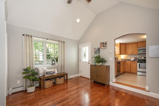 interior space featuring ceiling fan, arched walkways, high vaulted ceiling, light wood-style flooring, and a baseboard heating unit