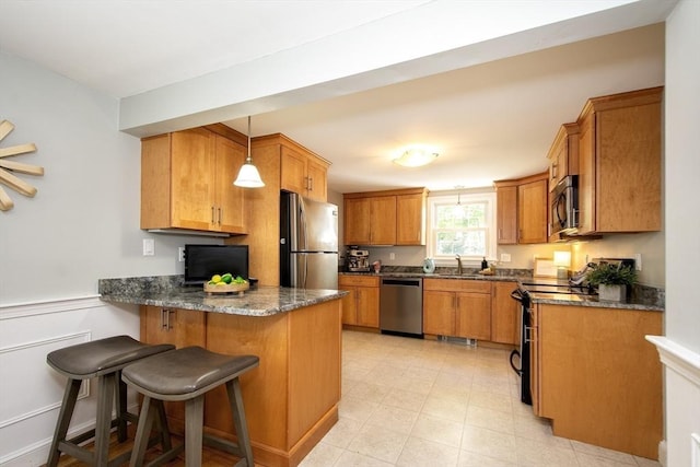 kitchen featuring pendant lighting, brown cabinets, a sink, a peninsula, and stainless steel appliances