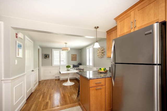 kitchen with freestanding refrigerator, wainscoting, brown cabinets, light wood finished floors, and decorative light fixtures