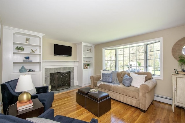 living area featuring a tiled fireplace, baseboard heating, light wood-type flooring, and built in shelves