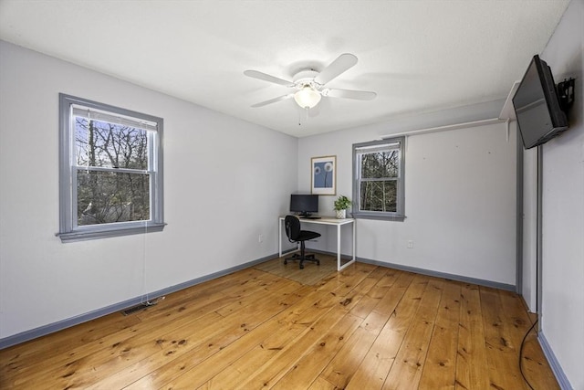 unfurnished office featuring ceiling fan, wood-type flooring, and a wealth of natural light