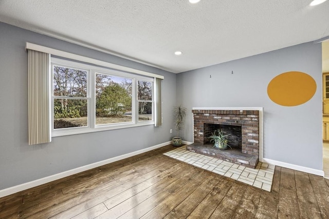 unfurnished living room with a brick fireplace, wood-type flooring, and a textured ceiling