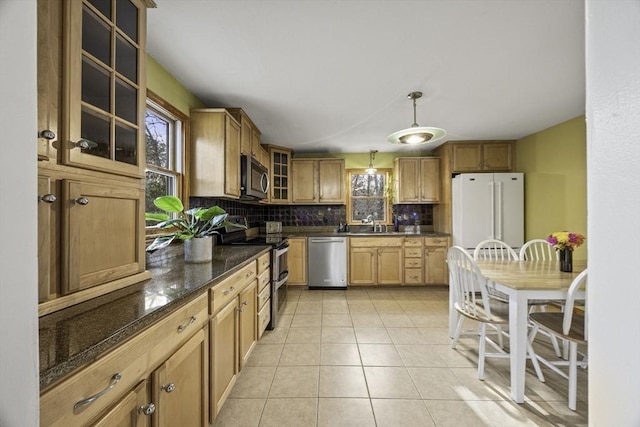 kitchen featuring stainless steel appliances, dark stone countertops, backsplash, hanging light fixtures, and light tile patterned floors