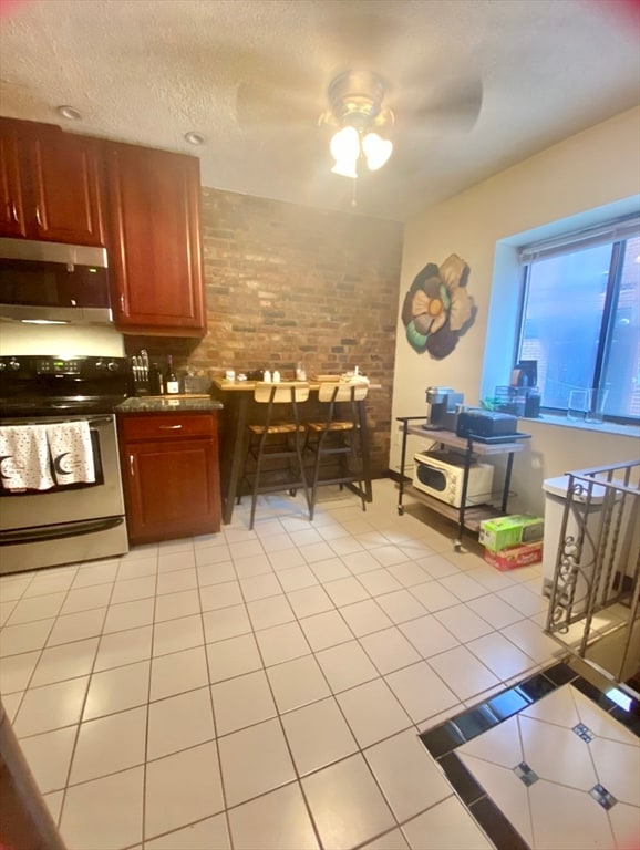 kitchen with ceiling fan, white electric range oven, brick wall, and light tile patterned floors