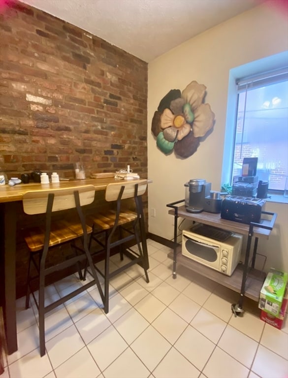 interior space featuring light tile patterned flooring and brick wall