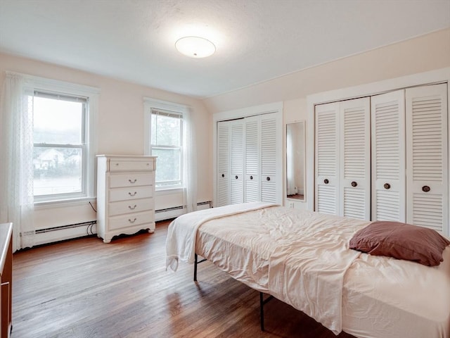 bedroom with lofted ceiling, hardwood / wood-style flooring, a baseboard heating unit, and multiple closets