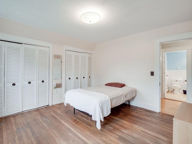 bedroom with multiple closets, connected bathroom, and hardwood / wood-style flooring