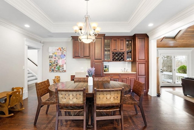 dining room with a chandelier, stairs, a tray ceiling, wet bar, and dark wood-style flooring