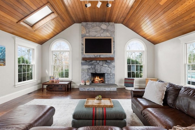 living room featuring a stone fireplace, vaulted ceiling with skylight, wood finished floors, and a wealth of natural light